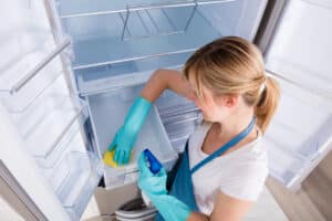 High Angle View Of Young Woman Cleaning Empty Refrigerator
